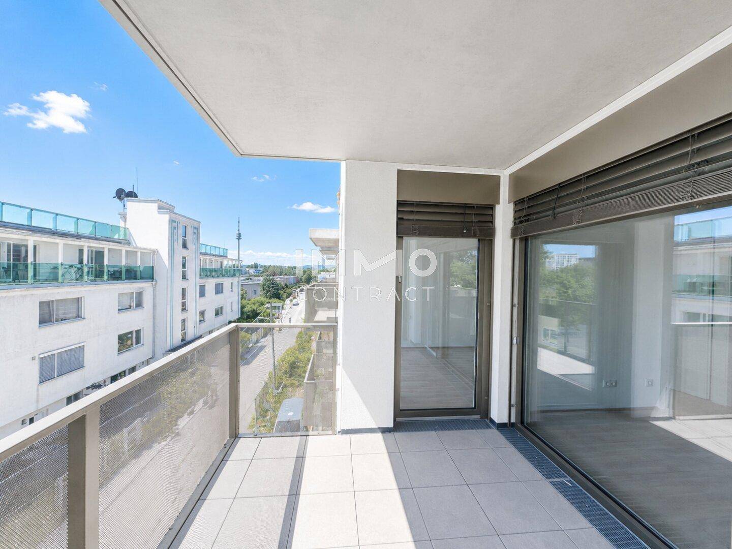 Geräumiger Balkon mit Fliesenboden und weitem Blick über die Stadt und umliegende Gebäude.