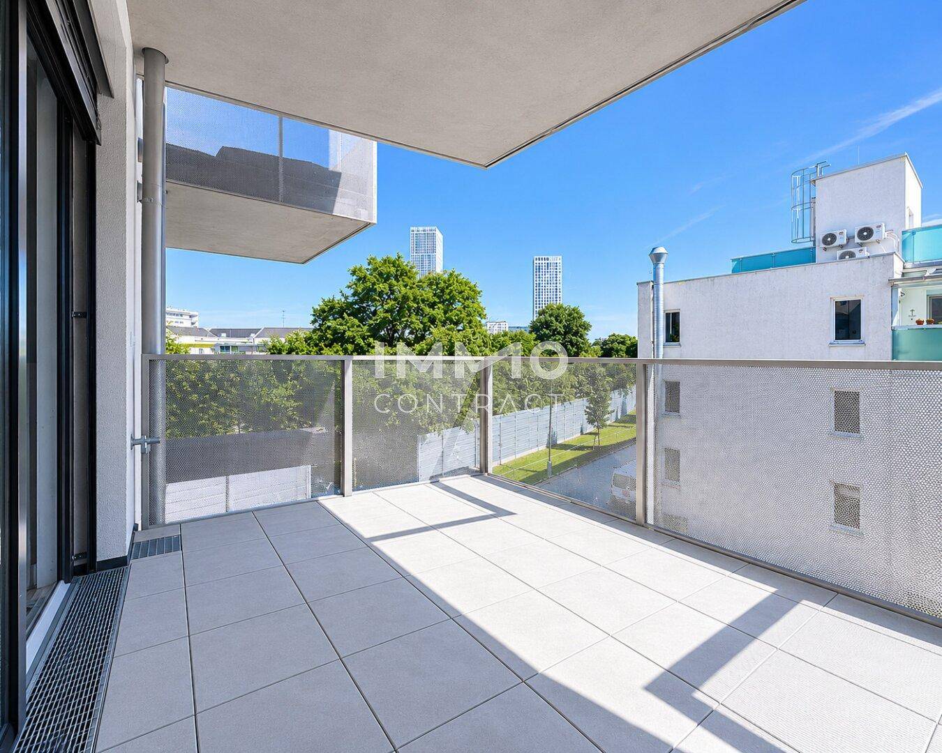 Heller Balkon mit Fliesenboden und Blick auf die Stadt, umgeben von modernen Gebäuden.