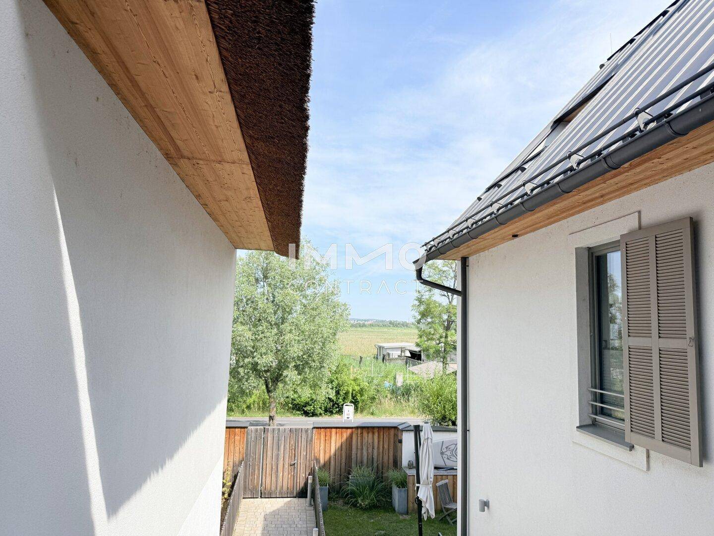 Blick zwischen zwei Gebäuden auf eine grüne Landschaft und den Himmel.
