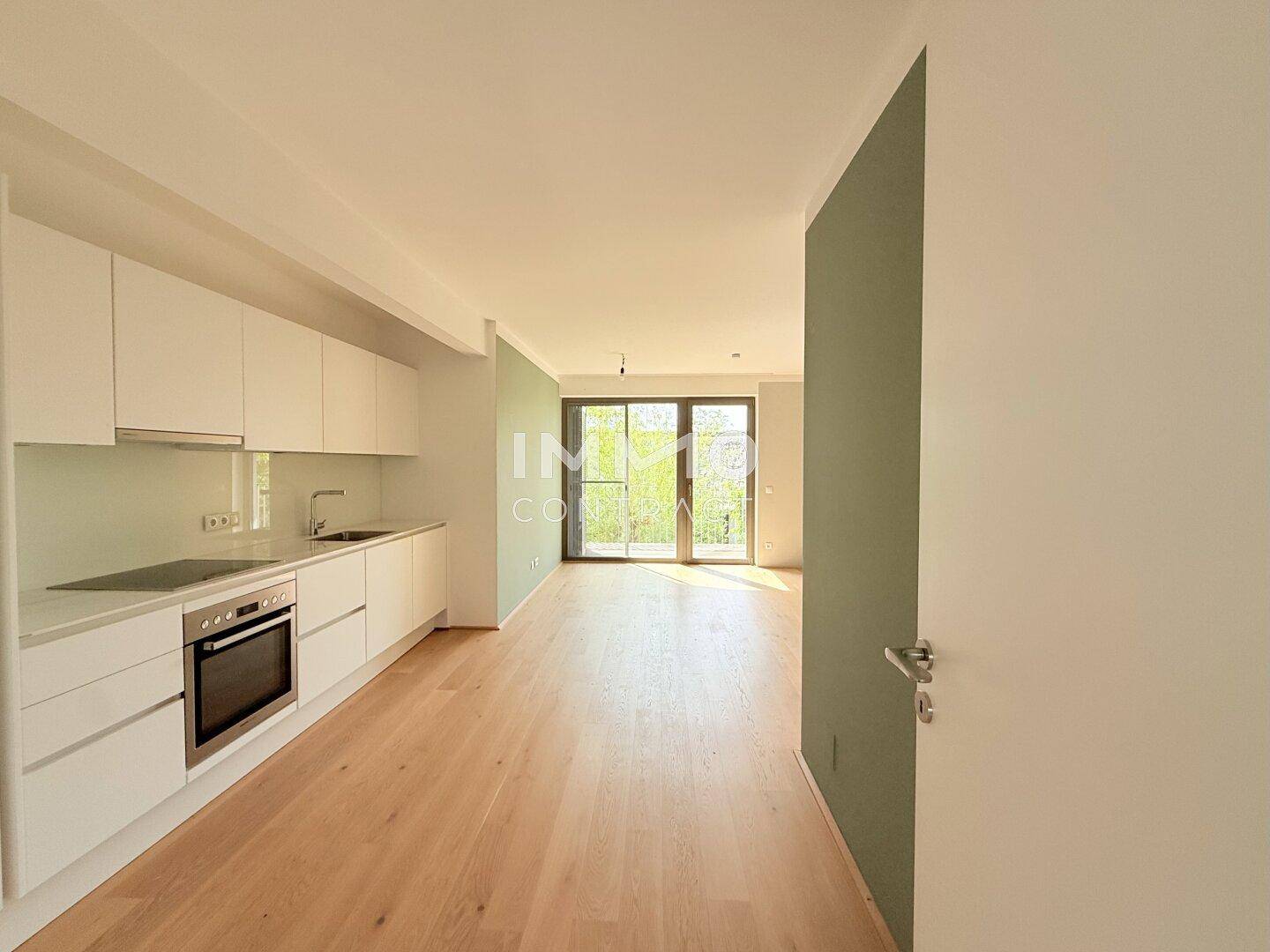 Offener Wohnbereich mit integrierter Küche und Zugang zu einem Balkon, auf Holzboden.