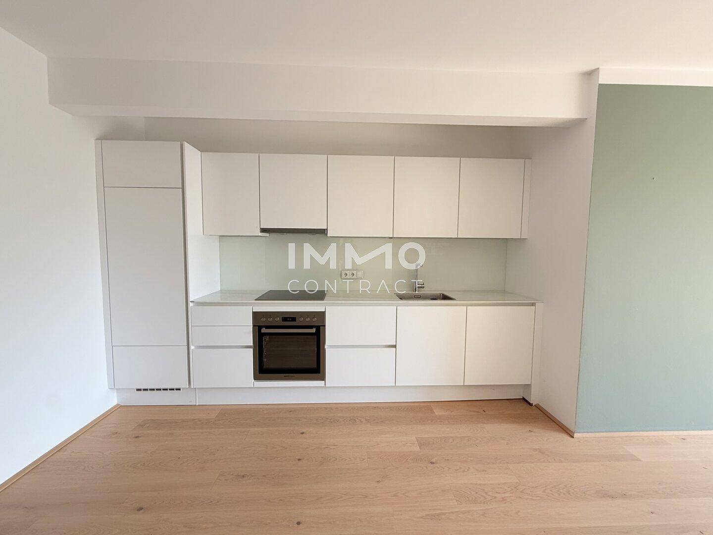 Neue, moderne Einbauküche mit weißen Fronten, Kochfeld und Backofen, auf Holzboden.