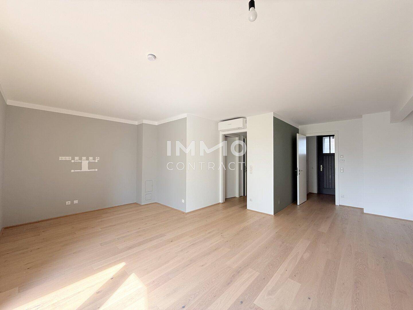 Heller Wohnbereich mit Holzboden und Zugang zu weiteren Räumen, in neutralen Farben gehalten.