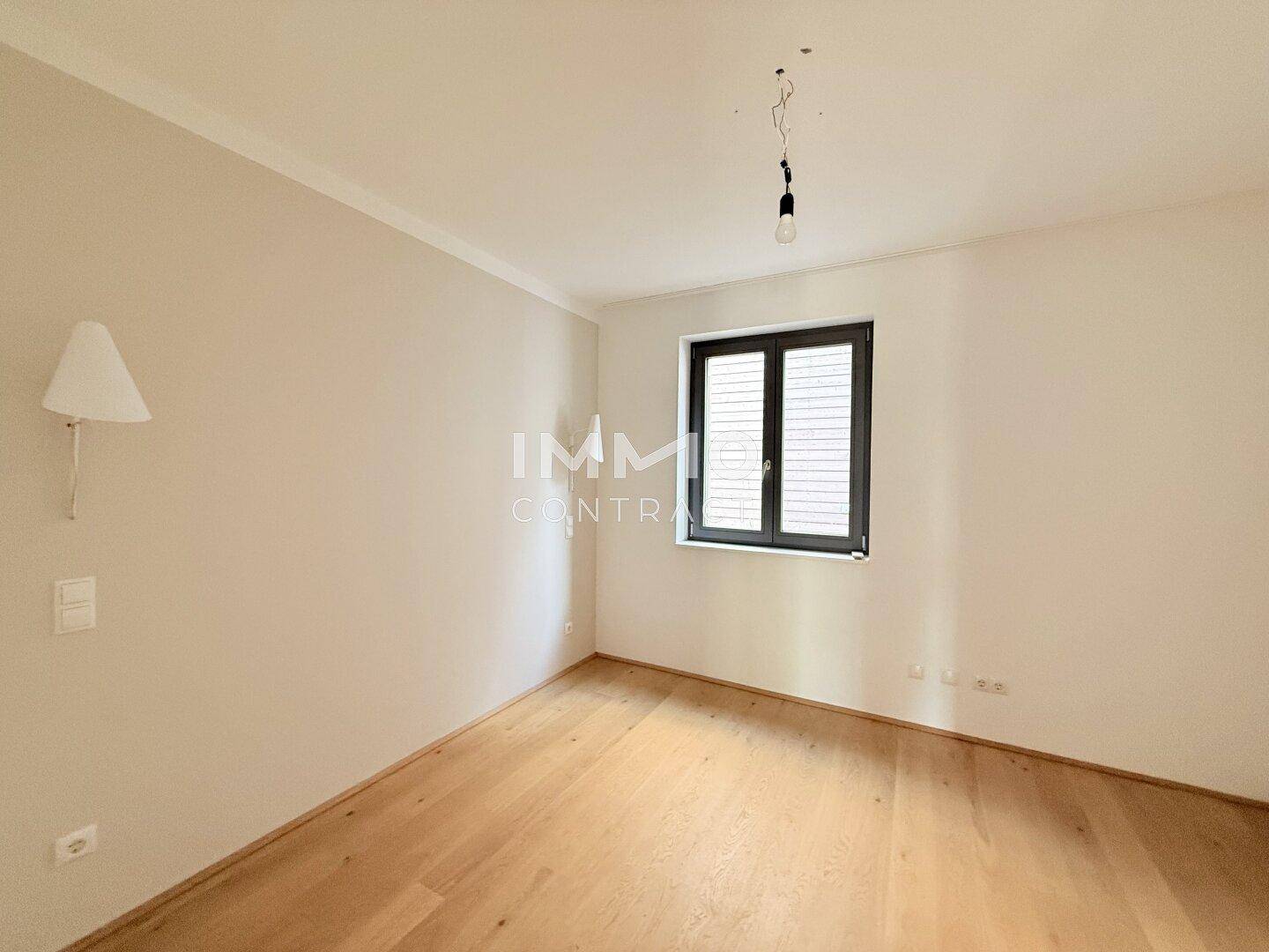 Schlafzimmer mit Holzboden und einem Fenster, das Tageslicht hereinlässt.
