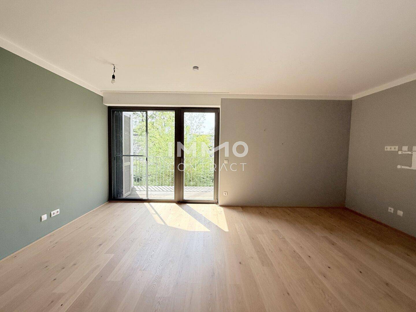 Geräumiges Wohnzimmer mit Holzboden und großen Fenstern, die viel Licht hereinlassen.