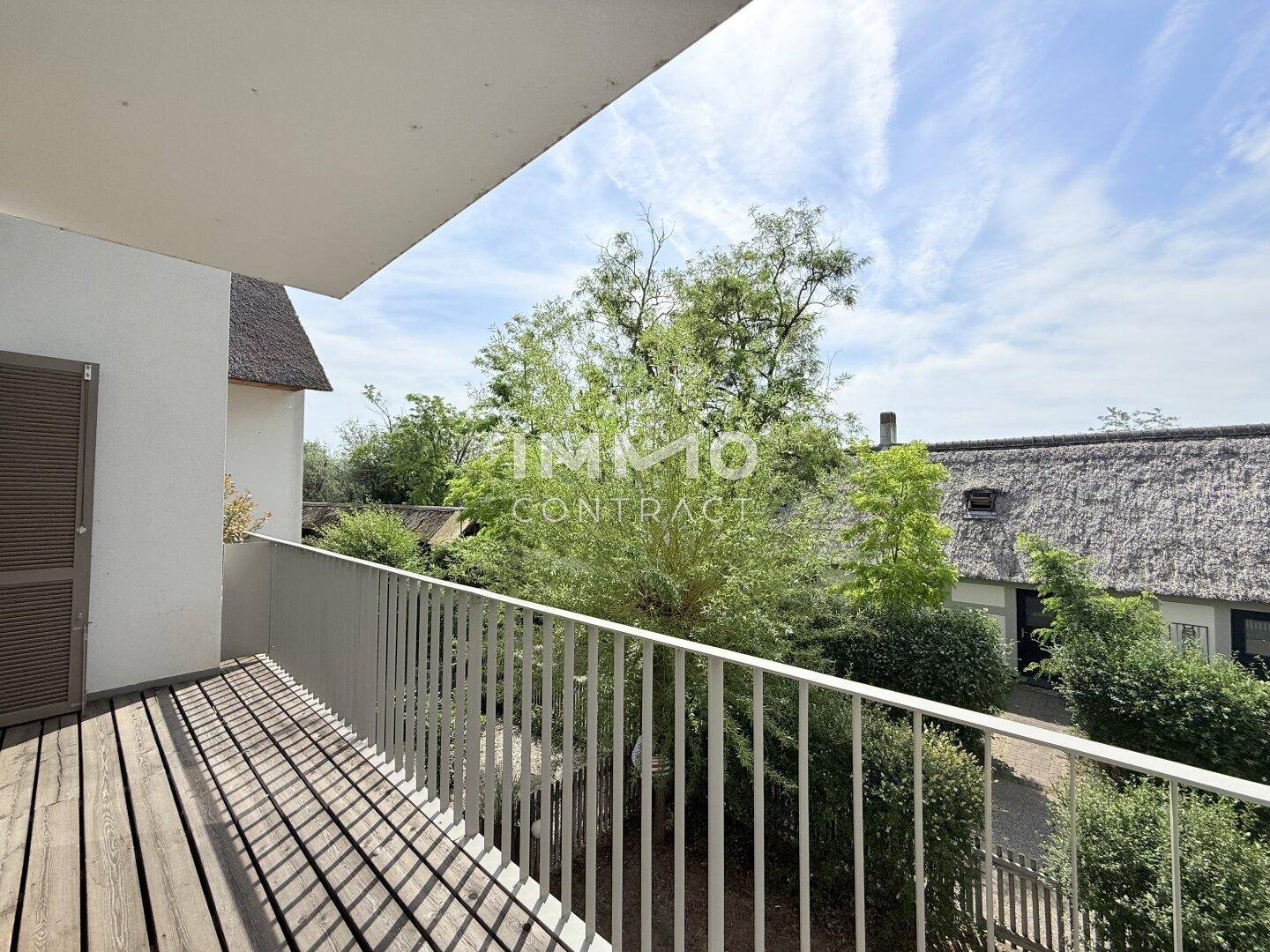 Balkon mit Holzboden und Blick auf grüne Bäume und traditionelle Reetdächer.