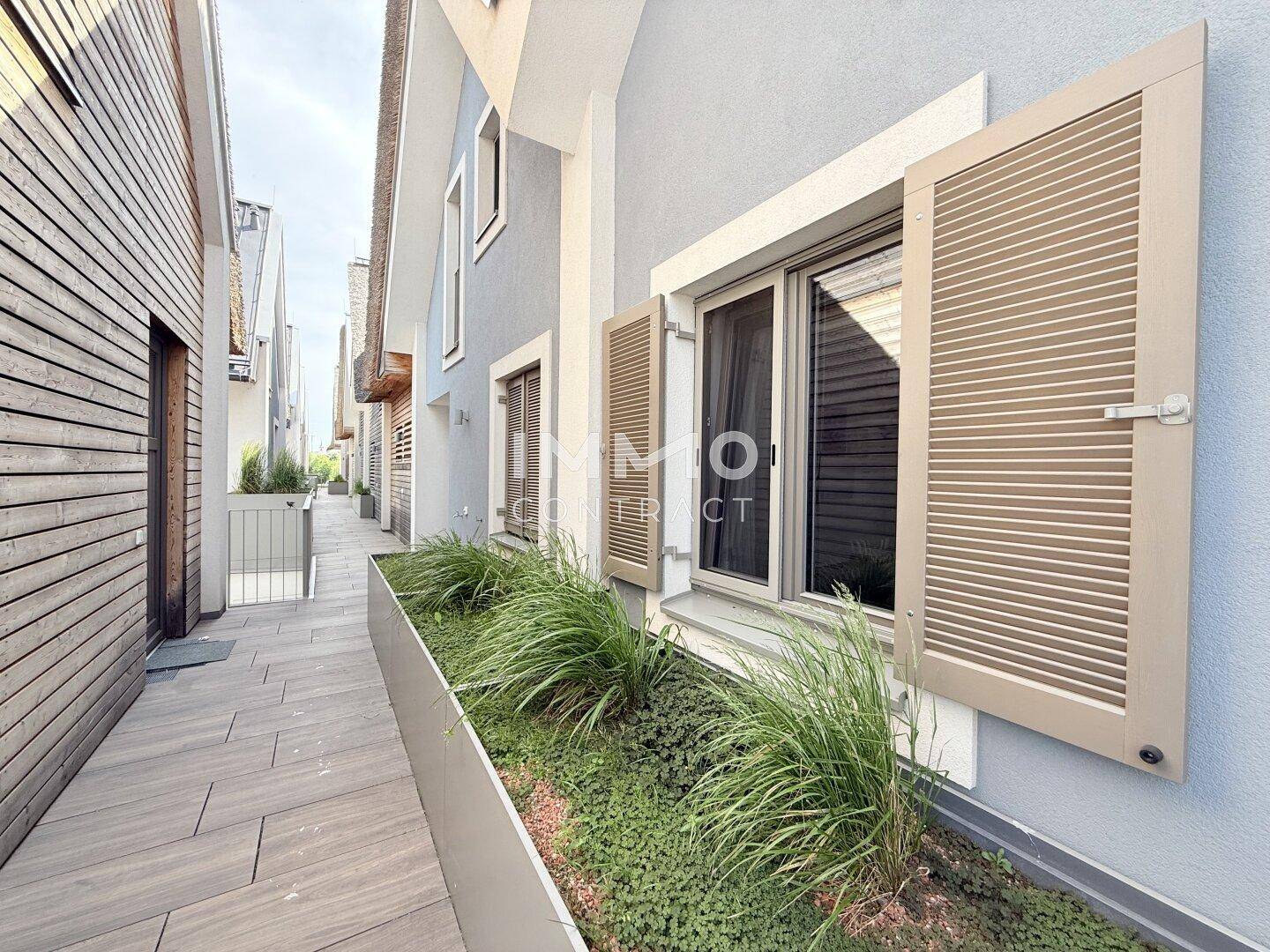 Außenansicht eines modernen Gebäudes mit Holzverkleidung und Fensterläden, umgeben von Grün.