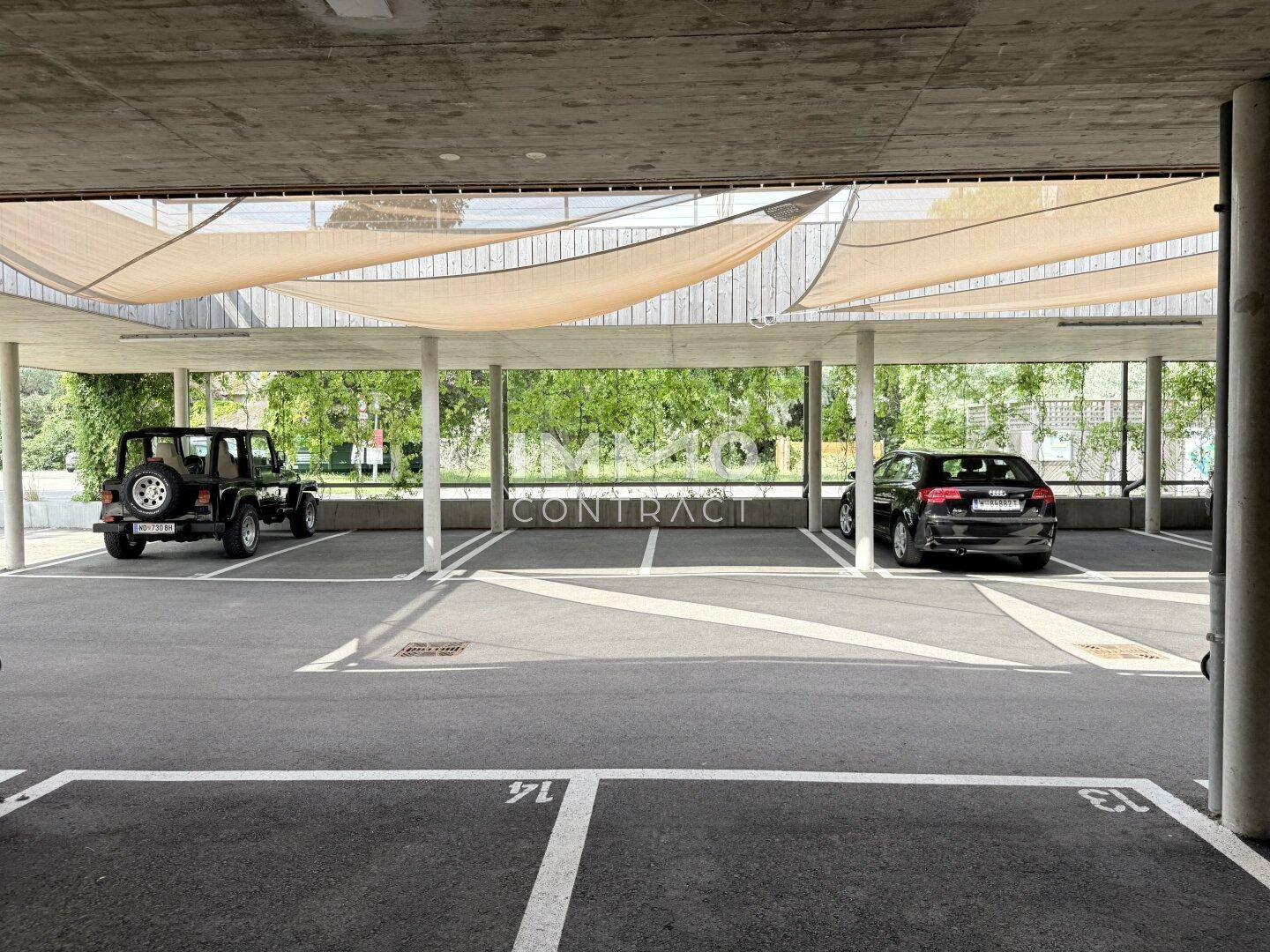 Überdachter Parkplatz mit mehreren Stellplätzen und Fahrzeugen, umgeben von Grün.