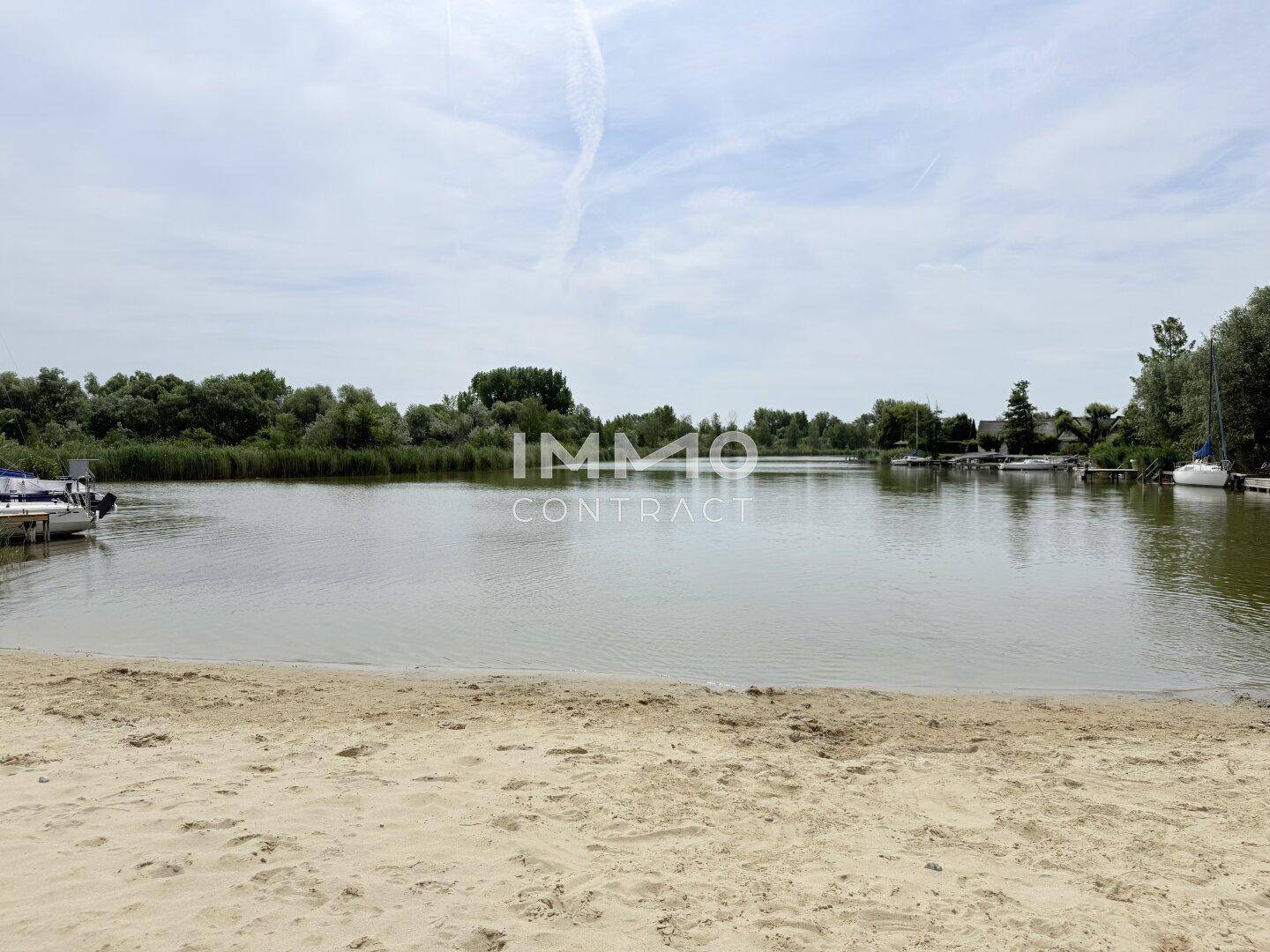 Ruhiger Seeabschnitt mit Sandstrand, umgeben von Schilf und Bäumen, ideal für Wassersport.