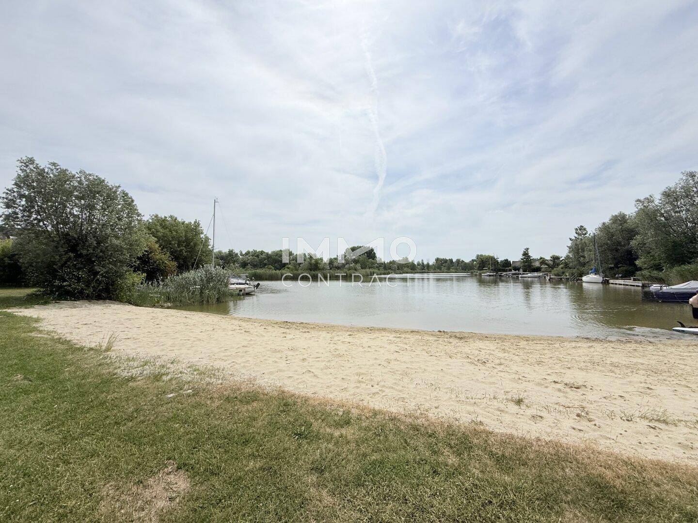 Idyllischer Sandstrand am Seeufer mit kleinen Booten und üppiger Vegetation im Hintergrund.