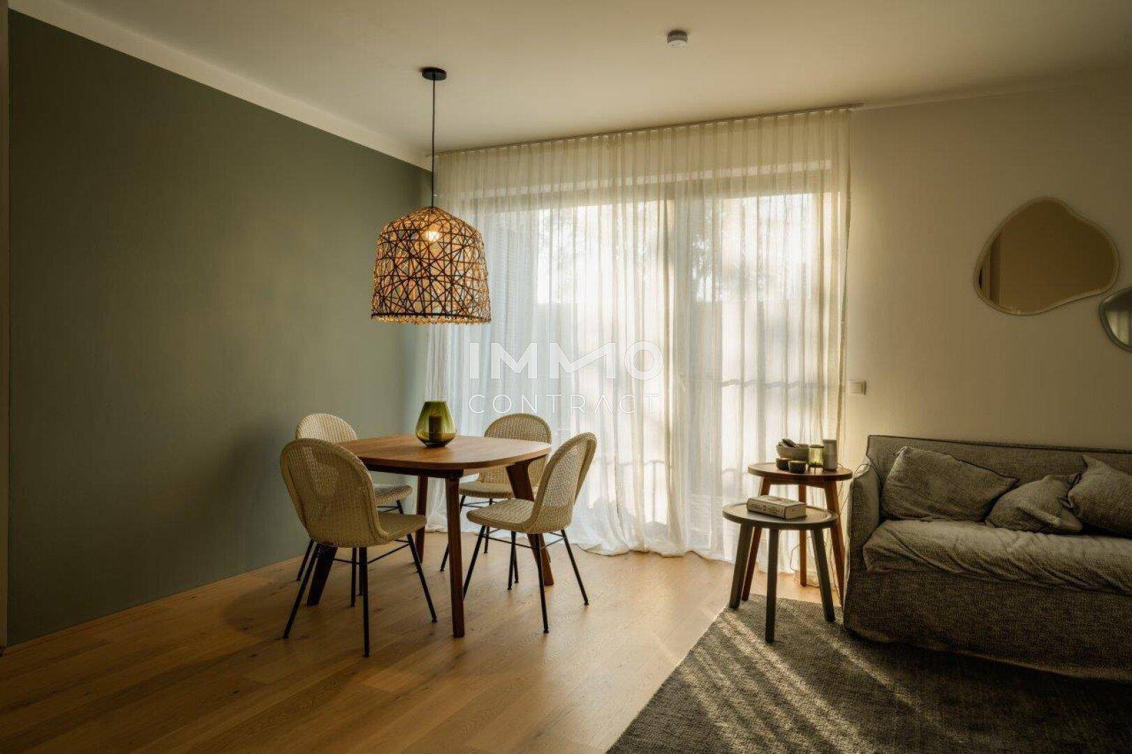 Heller Wohn-Essbereich mit Holzboden, Esstisch und Sofa, durch große Fenster lichtdurchflutet.