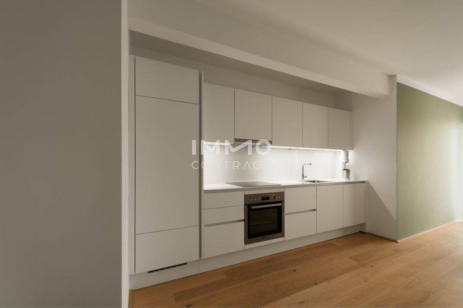 Moderne Einbauküche mit weißen Schränken, integrierten Geräten und Holzboden.