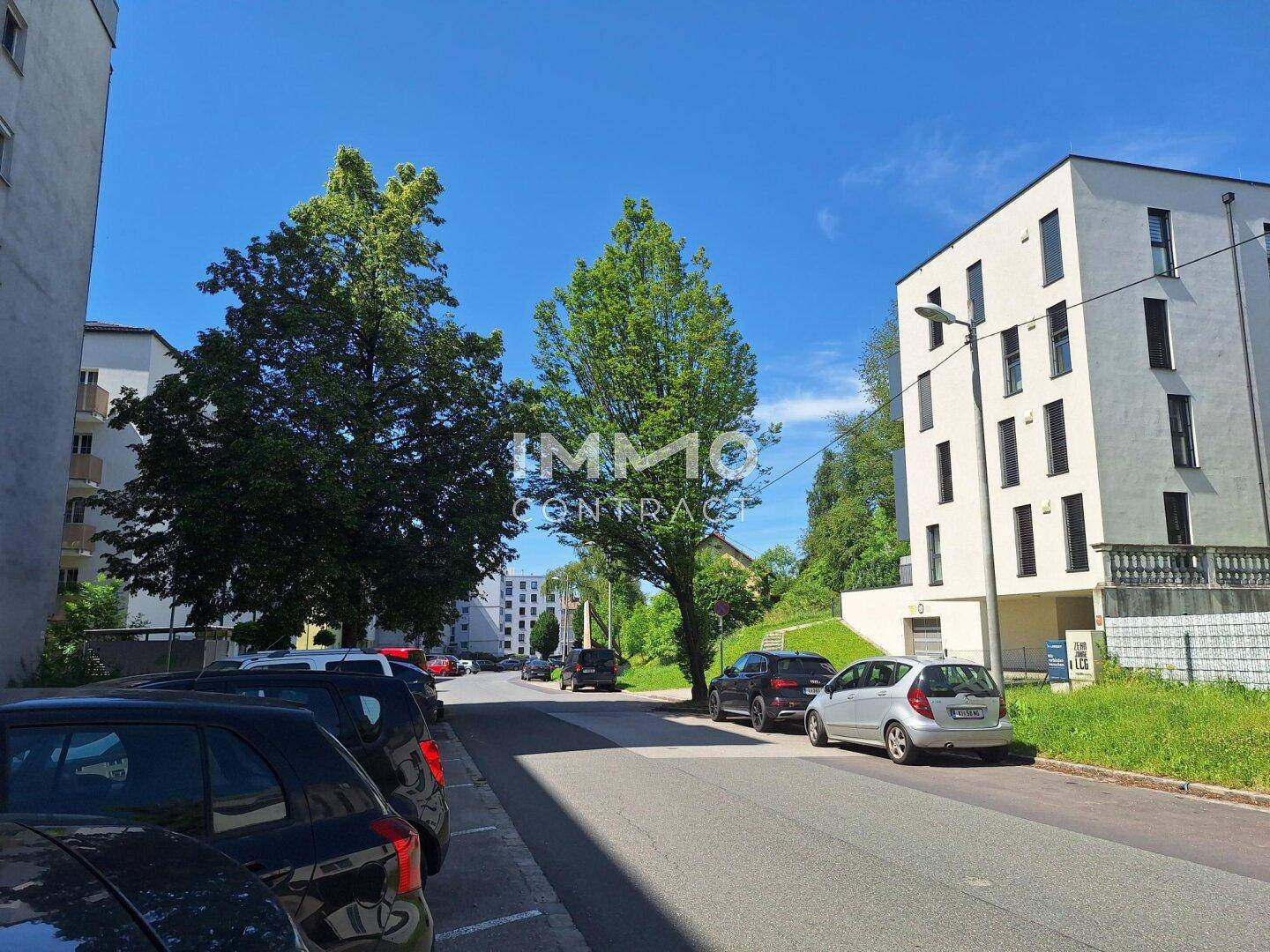 Wohngegend mit modernen Gebäuden, Bäumen und parkenden Autos unter blauem Himmel.