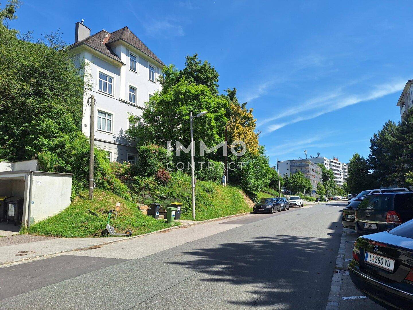 Ruhige Wohnstraße mit parkenden Autos und grünen Bäumen an einem sonnigen Tag.