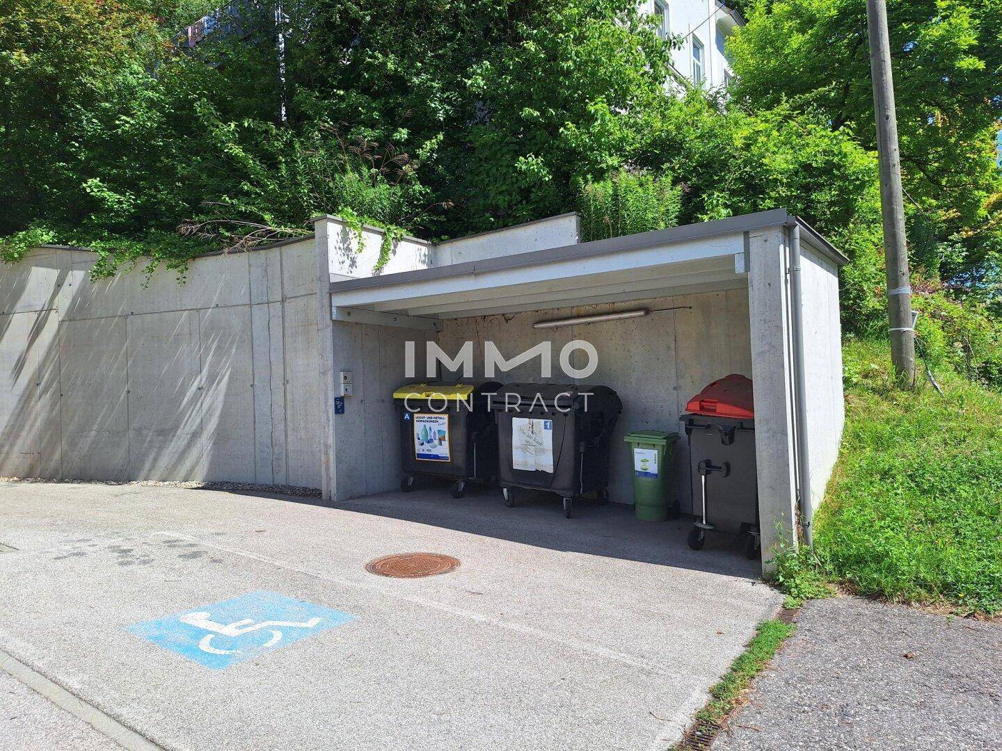 Überdachter Bereich für Mülltonnen mit Betonwänden und barrierefreiem Parkplatz.