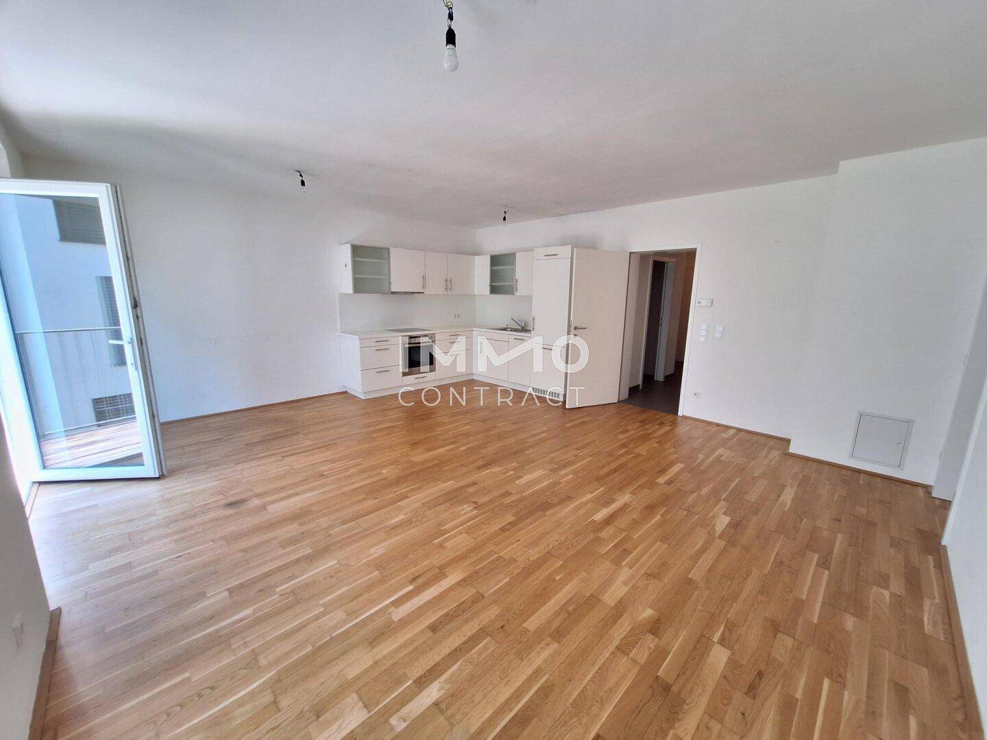 Heller Wohn-Essbereich mit integrierter Küche, Holzboden und Zugang zum Balkon.
