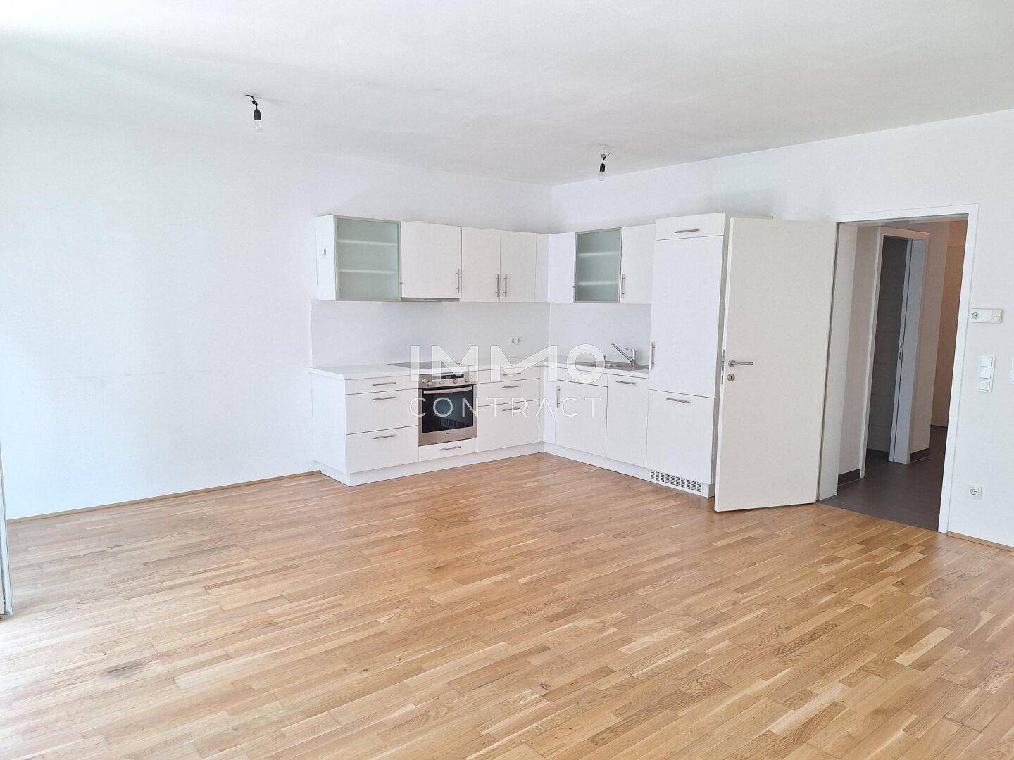 Moderne Einbauküche mit weißen Schränken und Holzboden in einem offenen Raum.