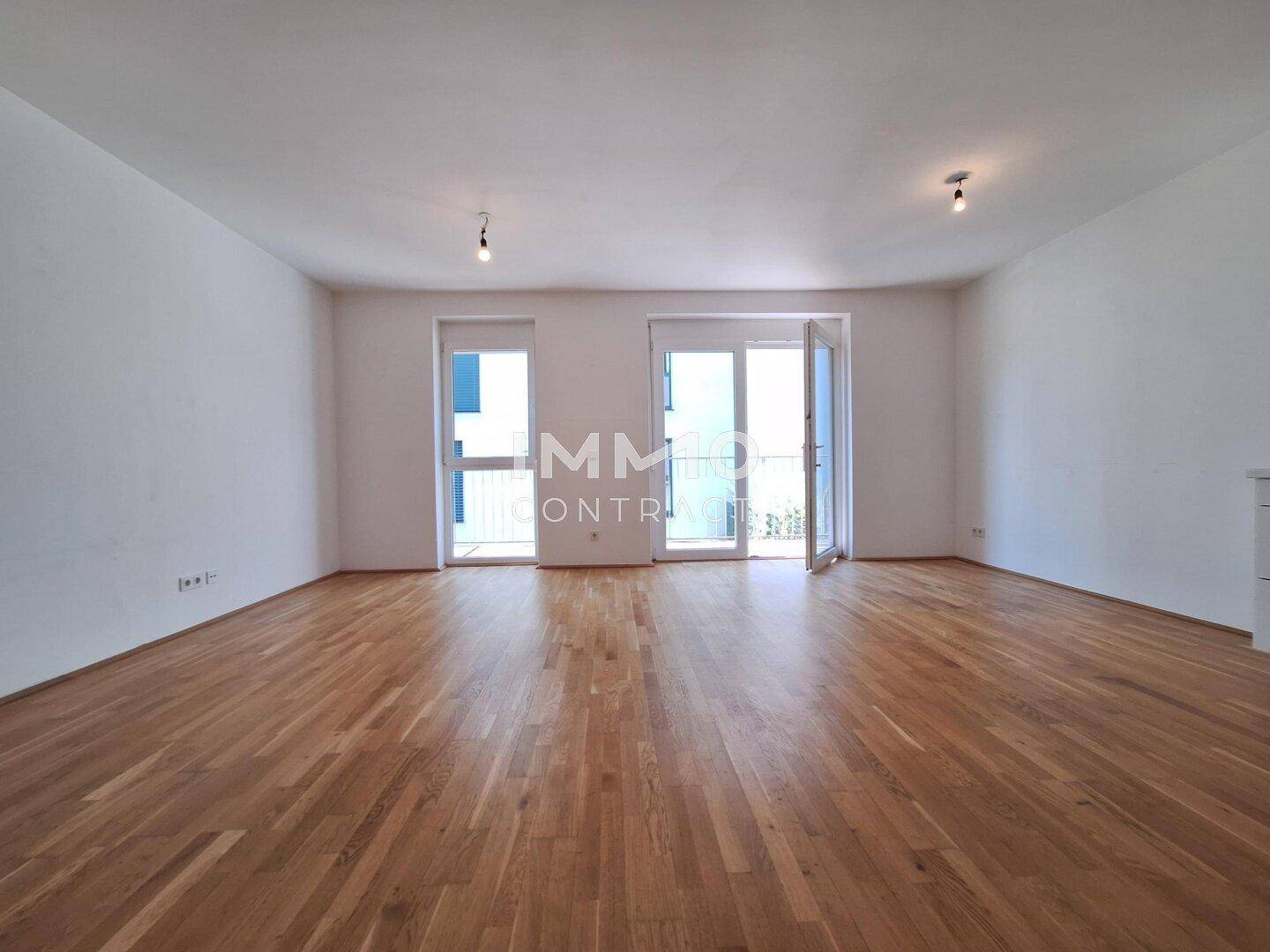 Geräumiges, leeres Wohnzimmer mit Holzboden und Zugang zu einem französischen Balkon.
