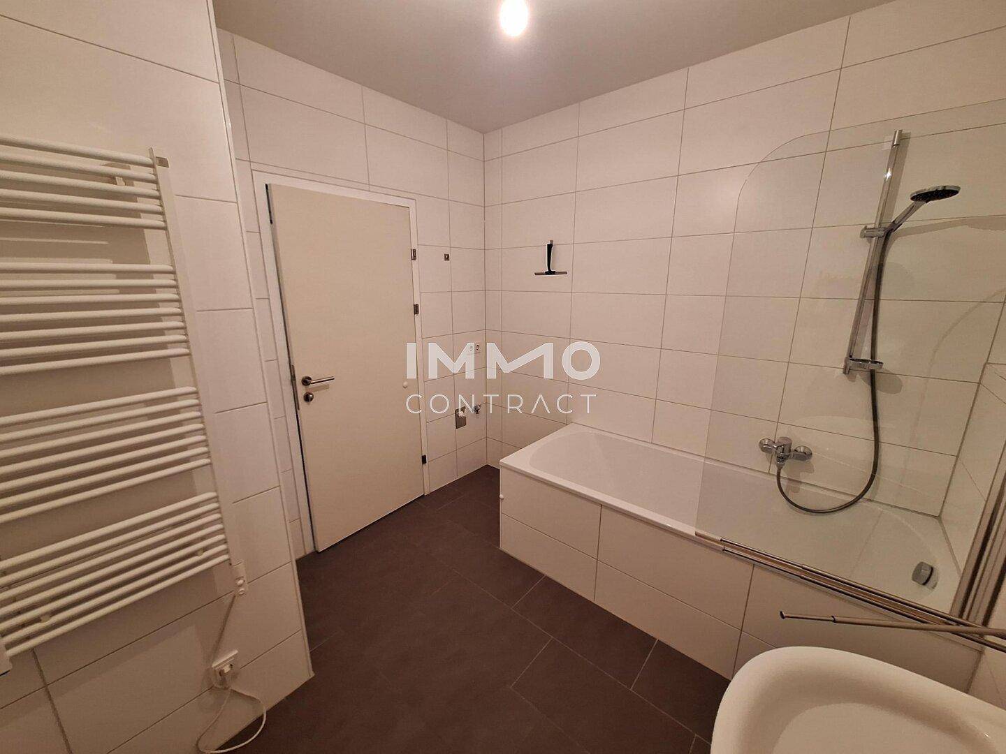 Modernes Badezimmer mit Badewanne, Duschbereich, weißen Fliesen und beheiztem Handtuchhalter.