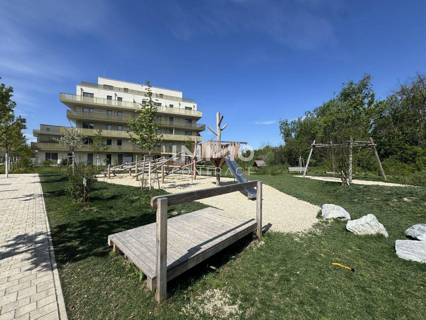 Wohngebäude mit einem Spielplatz im Vordergrund, umgeben von Grünflächen.