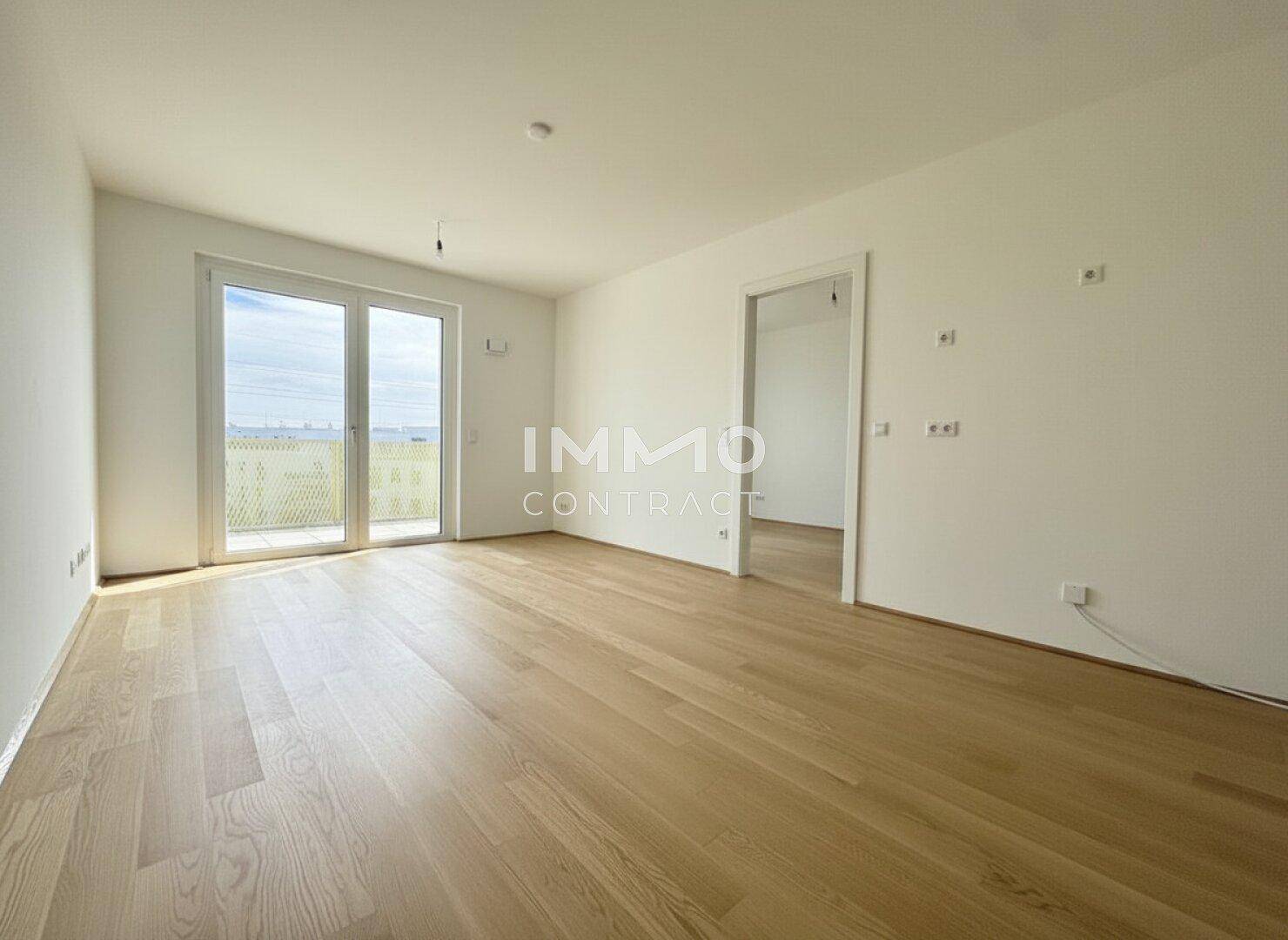 Geräumiges, leeres Zimmer mit Holzboden und einem offenen Durchgang zu einem weiteren Raum.
