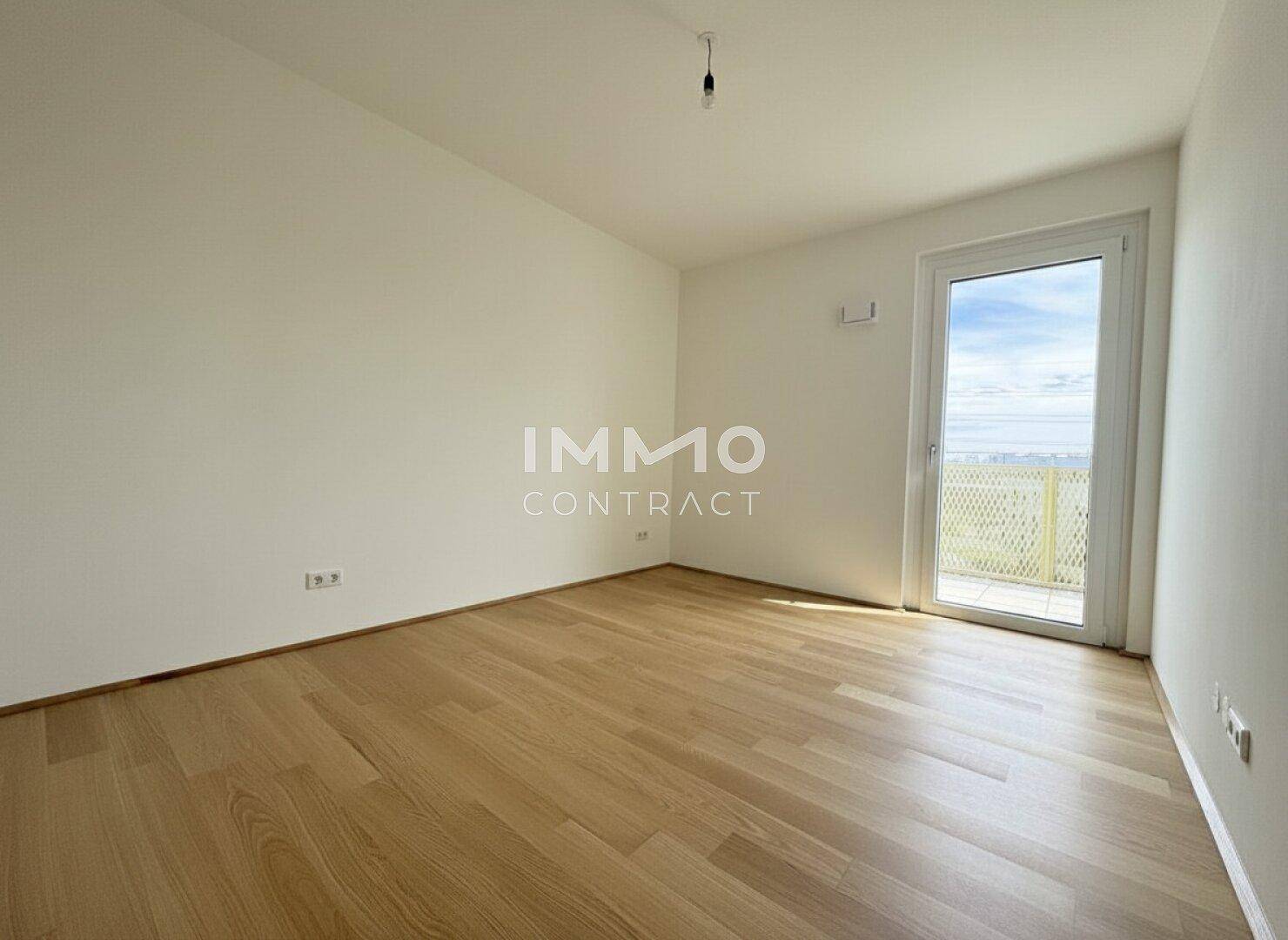 Leeres Schlafzimmer mit Holzboden und Zugang zu einem Balkon oder einer Terrasse.