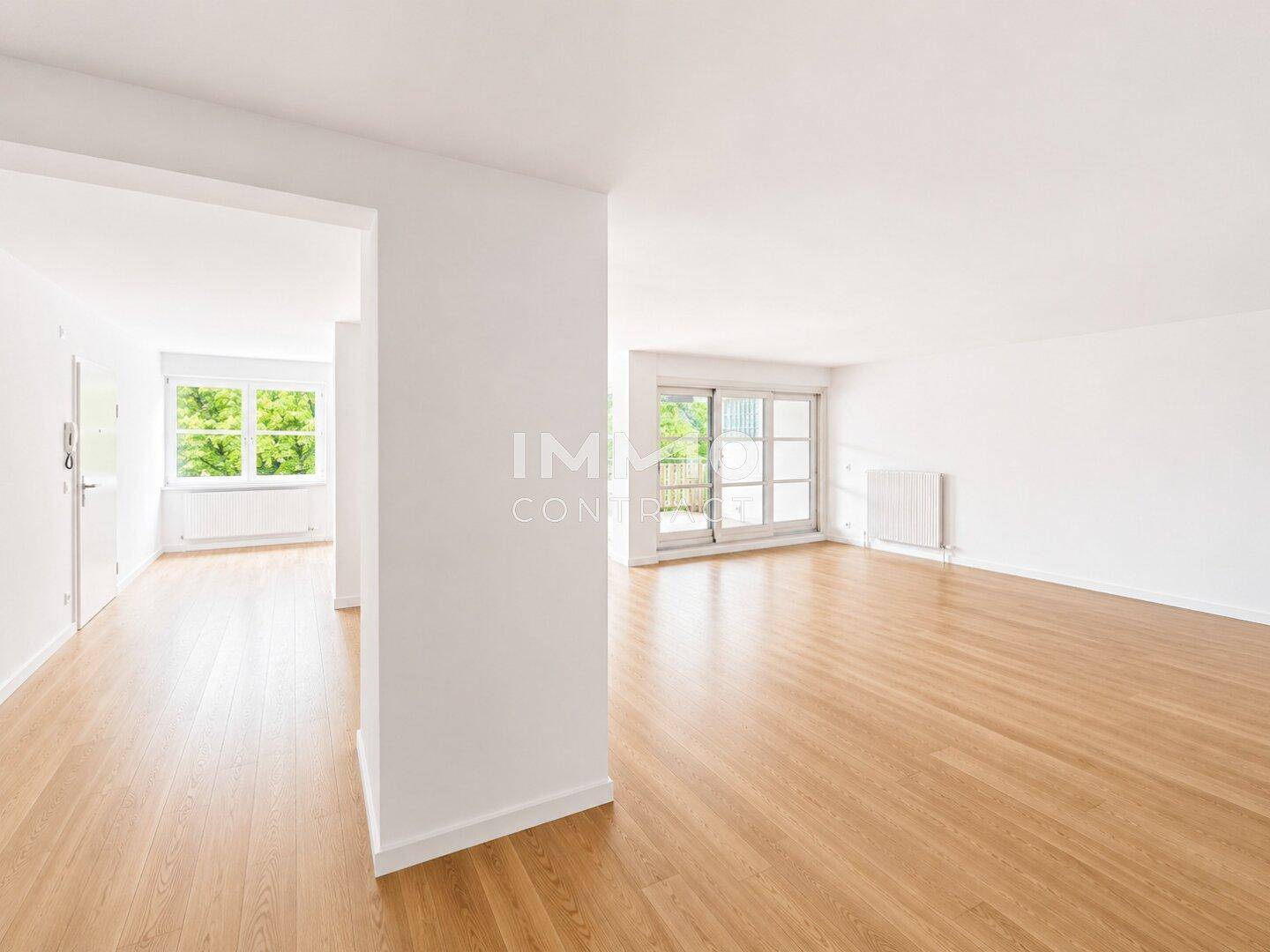 Lichtdurchfluteter Wohnbereich mit hellem Parkett und Zugang zu einem Außenbereich, umgeben von Bäumen.