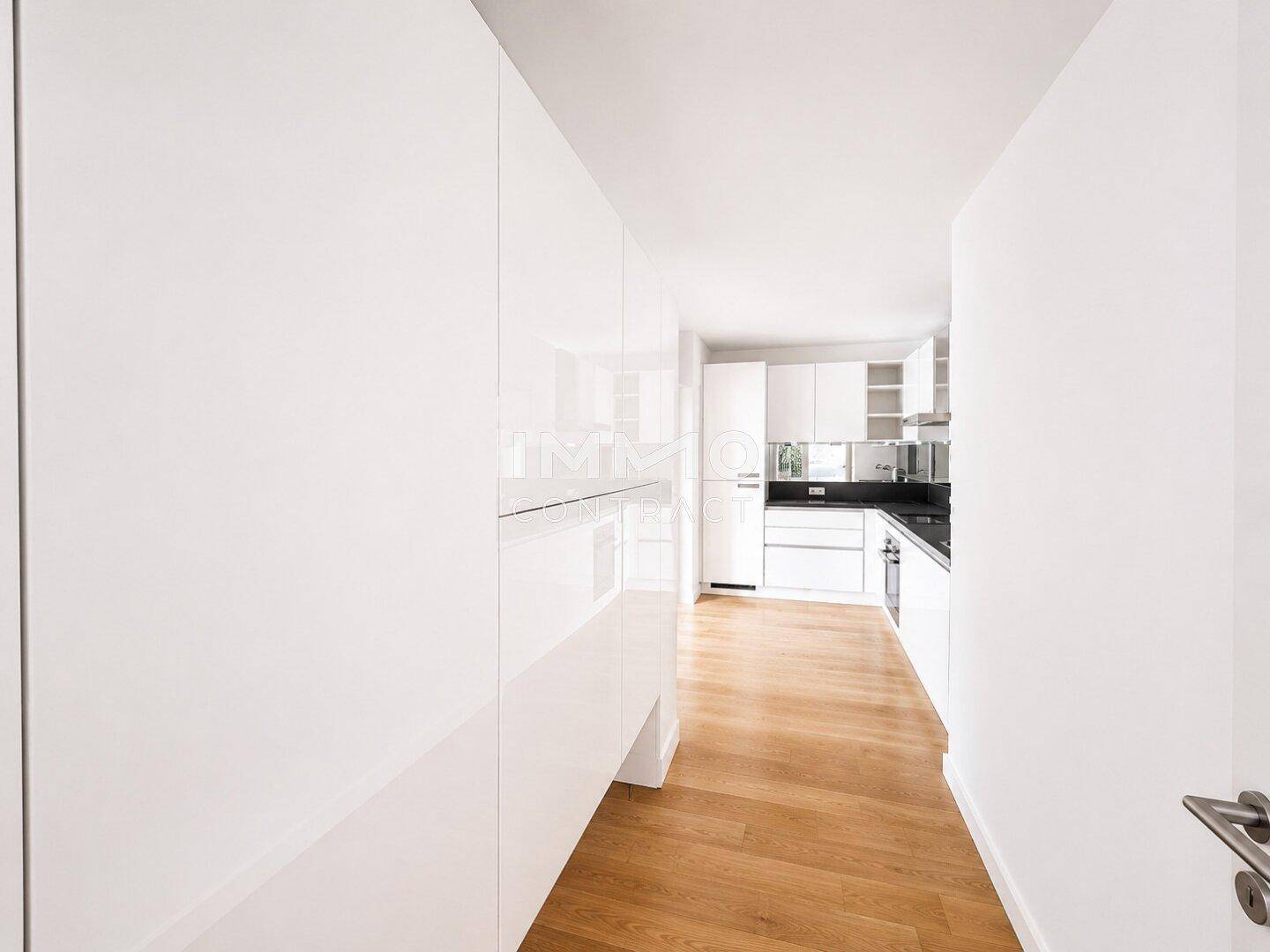 Moderne Küche mit weißen Hochglanzfronten, dunkler Arbeitsplatte und integrierten Geräten.