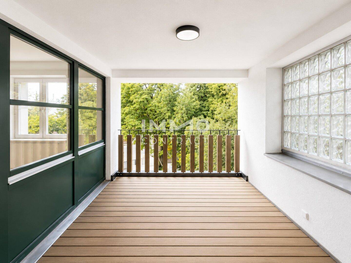 Überdachte Loggia mit Holzdeck, Glasbausteinen und Blick auf grüne Bäume.