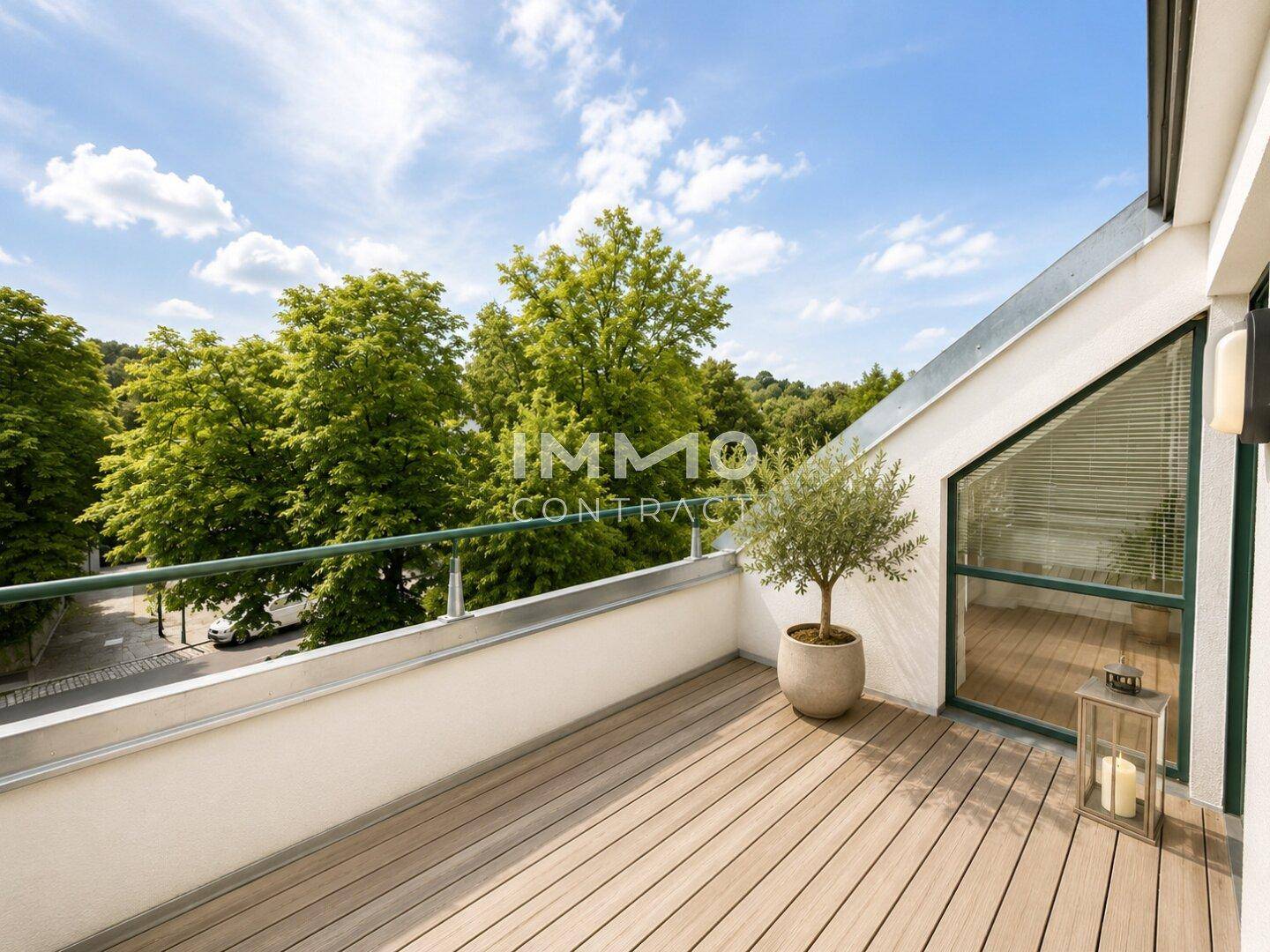 Sonniger Balkon mit Holzdeck, Topfpflanze und weitem Blick über grüne Baumwipfel.