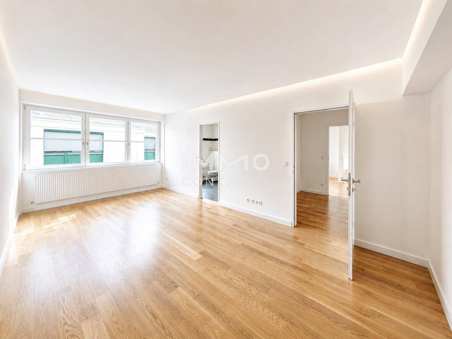 Geräumiger, heller Raum mit Parkettboden, großen Fenstern und indirekter Deckenbeleuchtung.