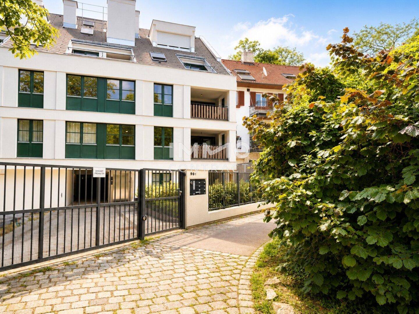 Eingangsbereich eines modernen Mehrfamilienhauses mit Zufahrtstor und gepflegten Büschen.