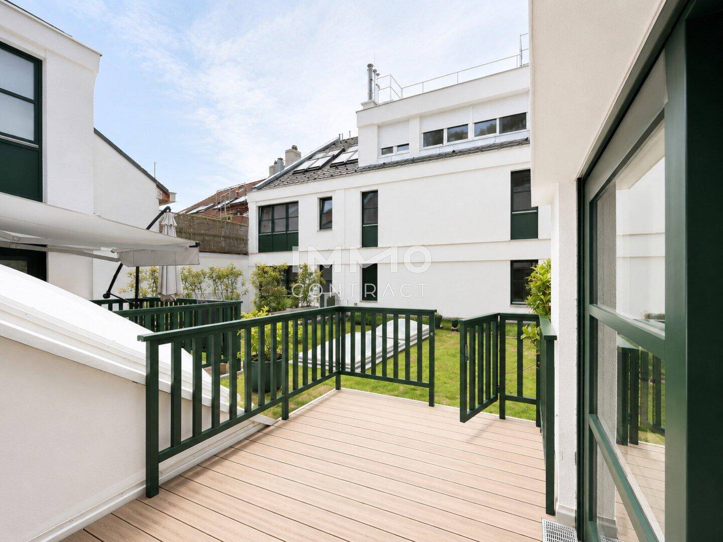 Kleiner Balkon mit Holzboden und Blick auf den Gemeinschaftsgarten und umliegende Gebäude.