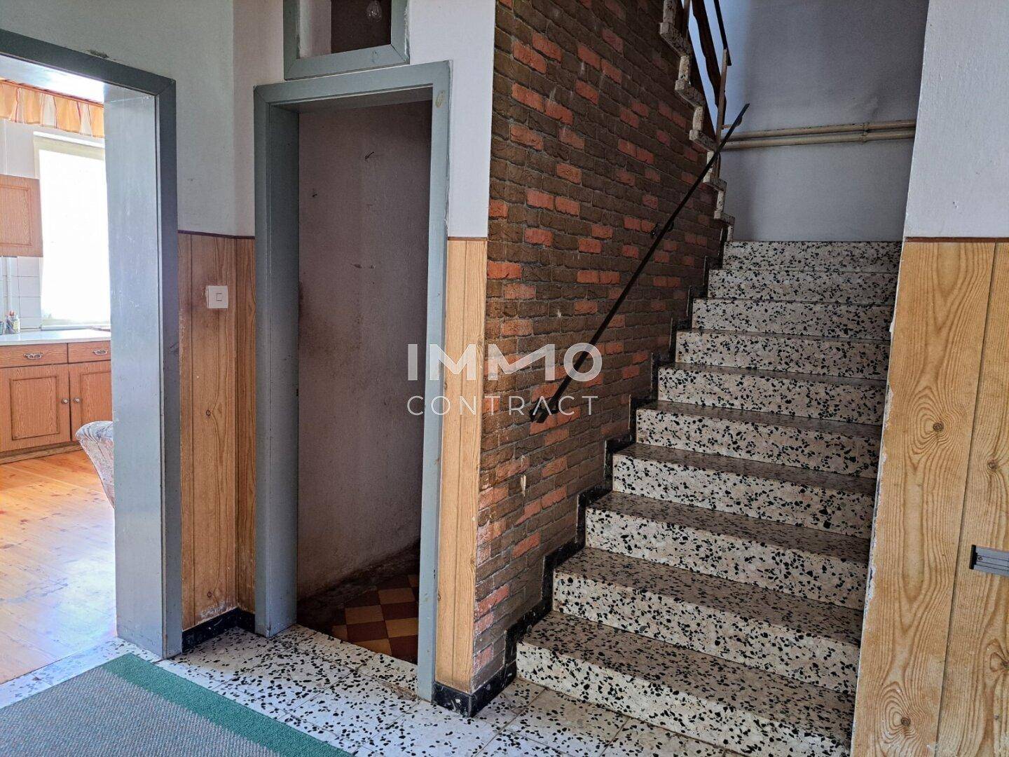 Treppenhaus mit Terrazzostufen, Ziegelwand und Zugang zu weiteren Räumen.