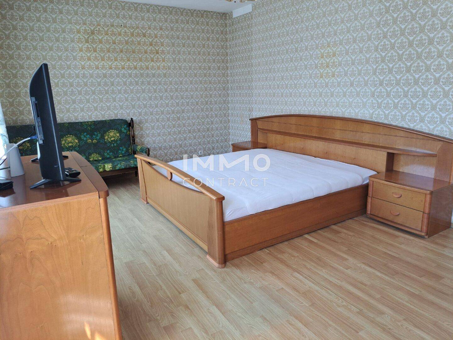 Schlafzimmer mit Holzbett, Laminatboden und gemusterter Tapete in hellem Ambiente.
