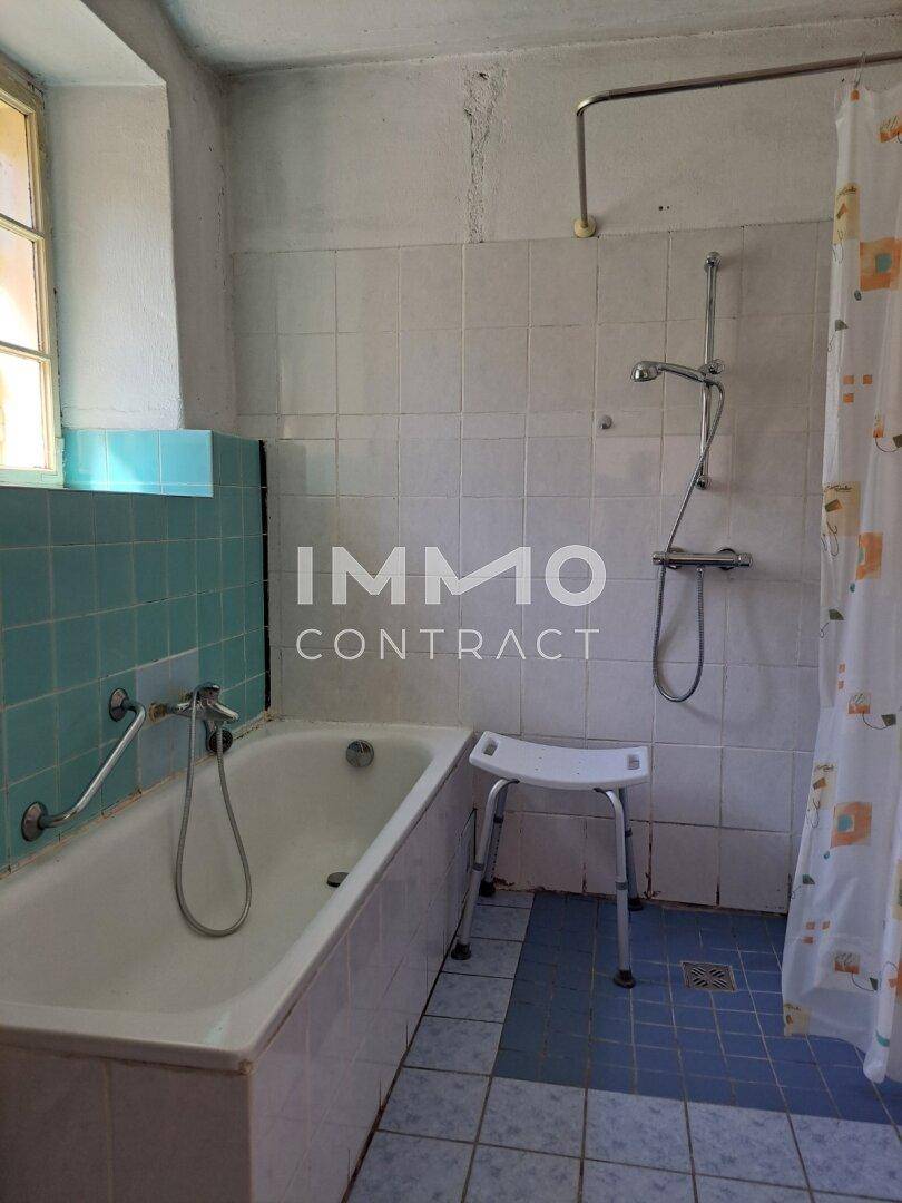 Badezimmer mit Badewanne, blauen Fliesen und Fenster in älterem Zustand.