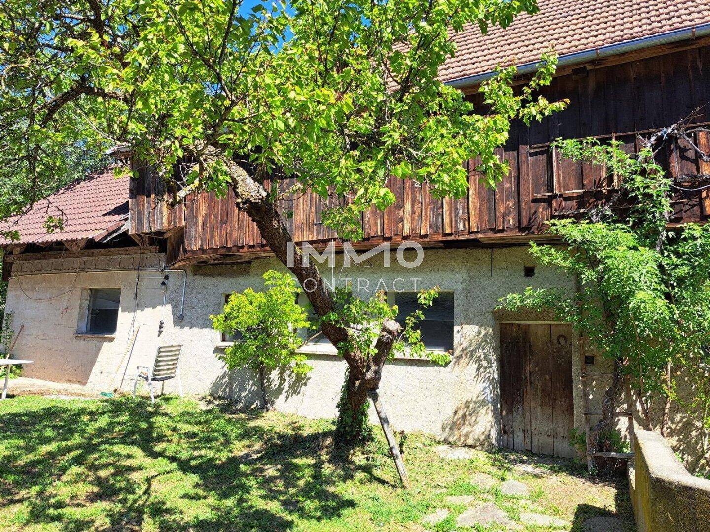 Fassade eines alten Gebäudes mit Garten, Bäumen und Holzbalkon.