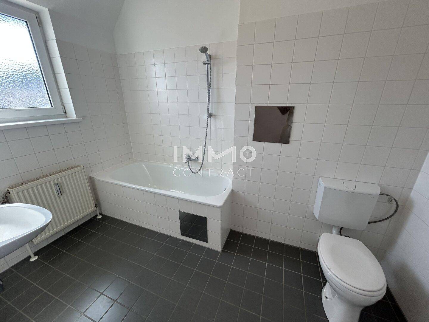 Helles Badezimmer mit Badewanne, WC, Waschbecken und Fenster, ausgestattet mit weißen Fliesen.