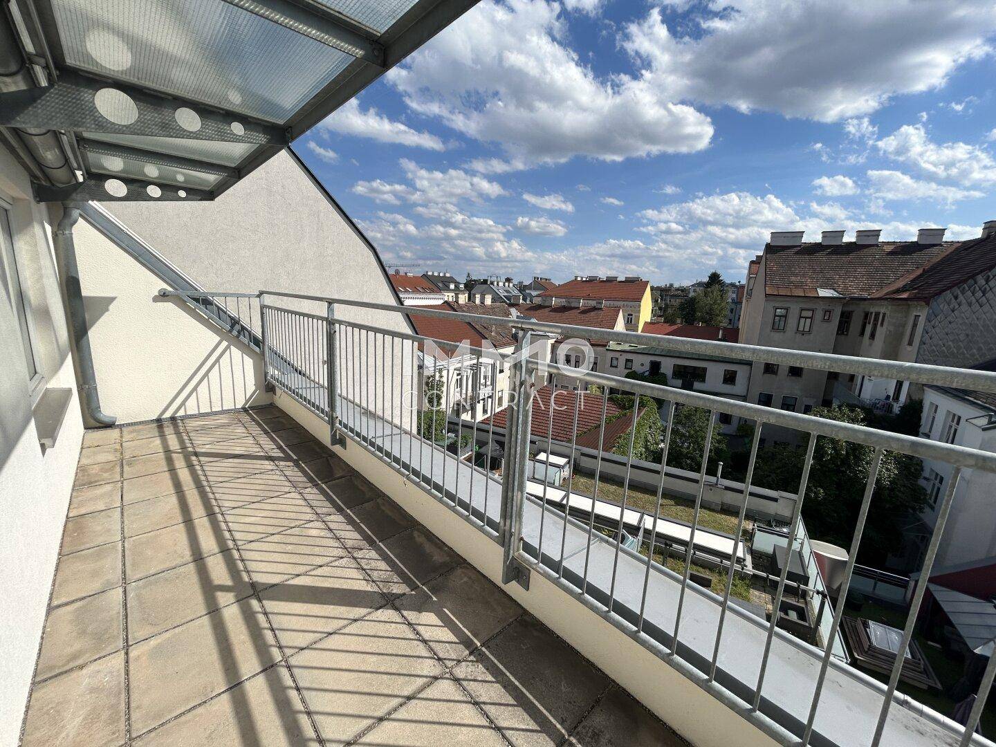 Überdachter Balkon mit Fliesenboden und Blick auf die umliegenden Stadtgebäude, ideal zum Entspannen.