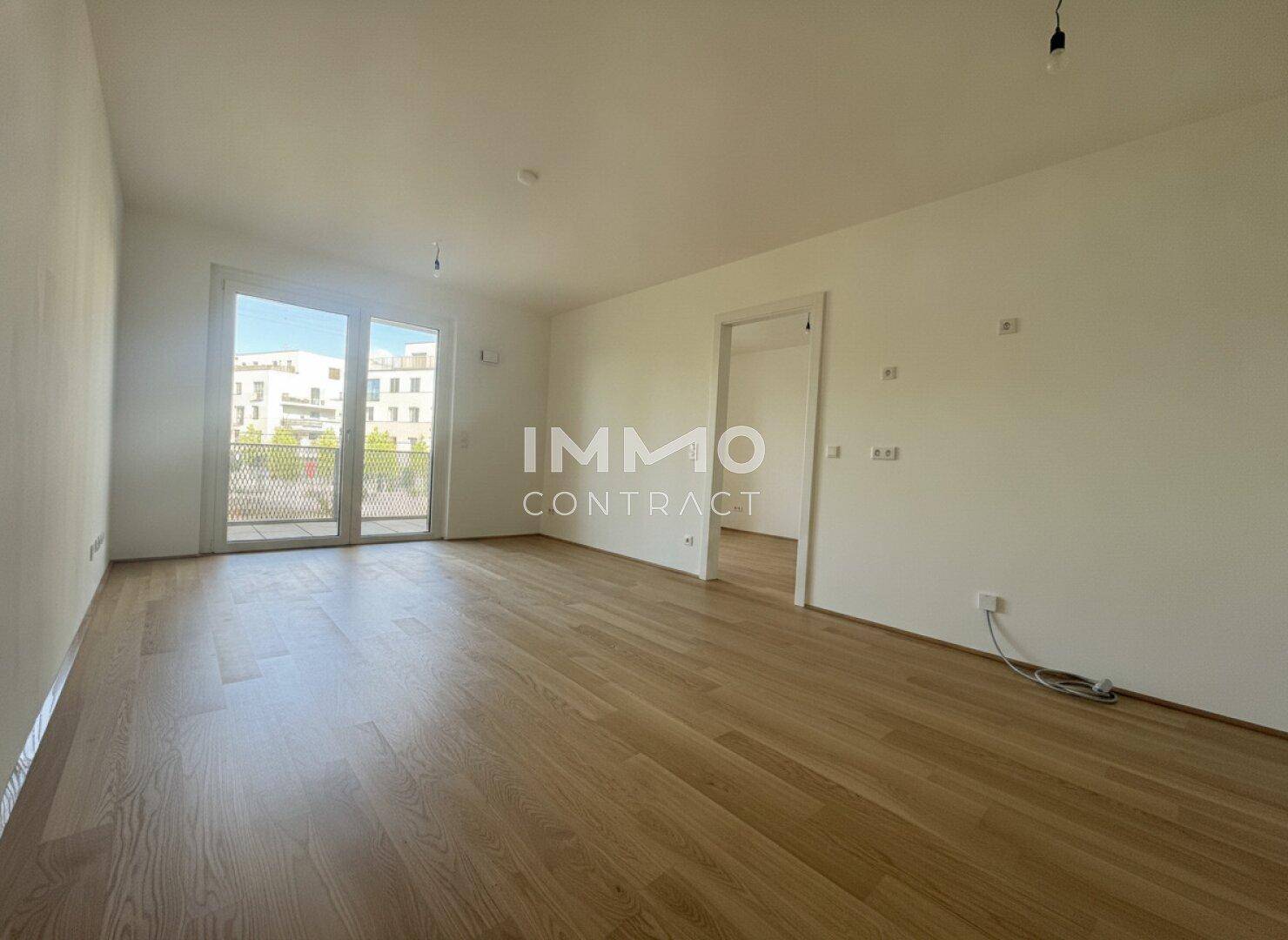 Heller, leerer Raum mit Holzboden und Zugang zu einem Balkon.