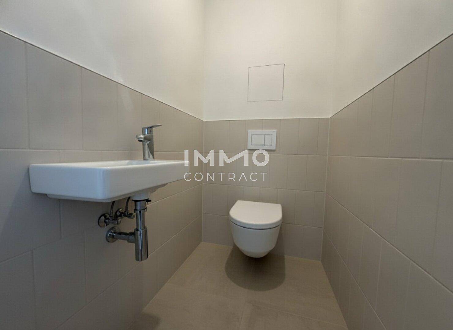 Modernes Gäste-WC mit Wand-WC und kleinem Waschbecken in hellen Fliesen.