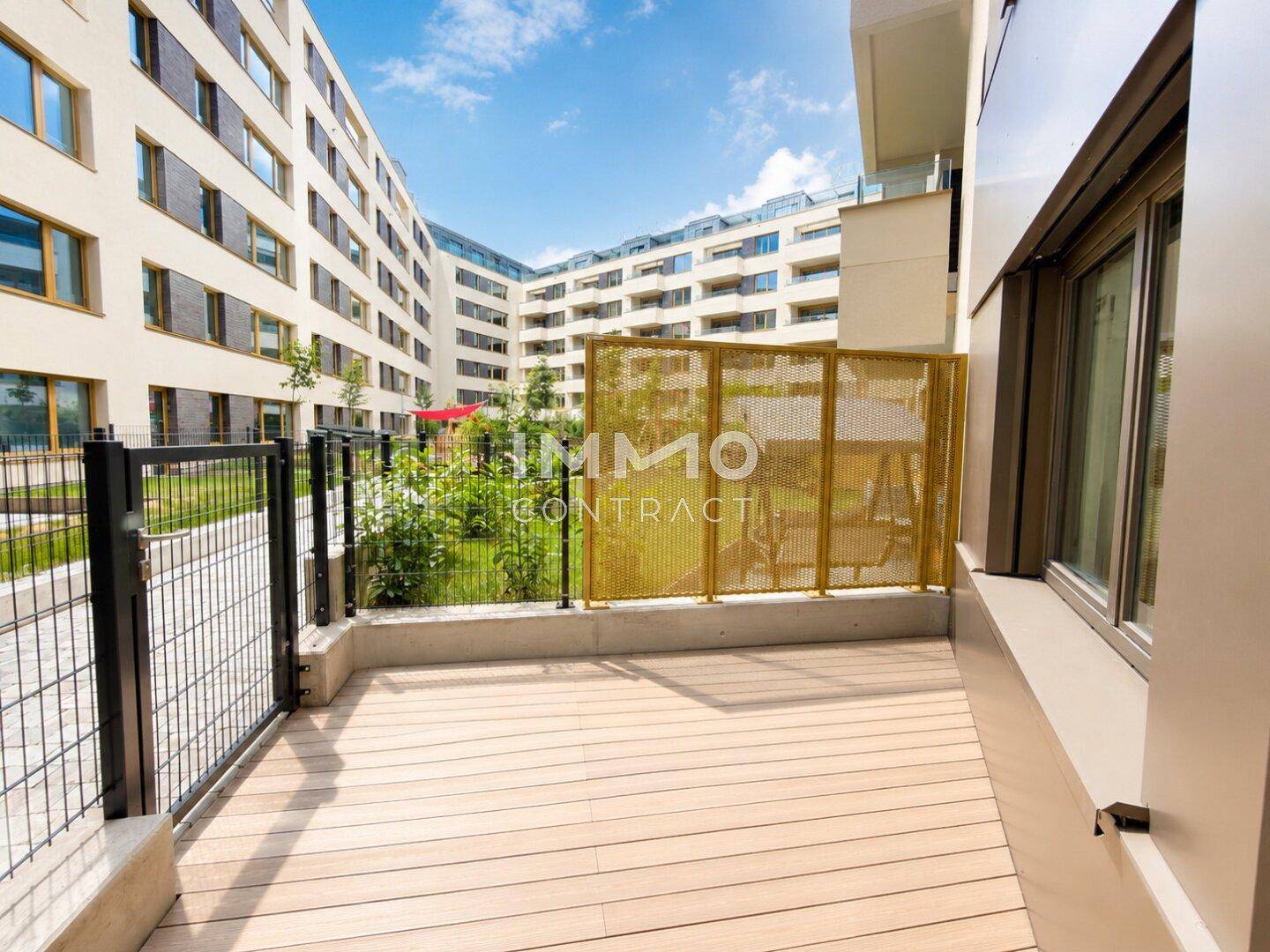 Erdgeschoss-Terrasse mit Holzdeck und Blick auf den begrünten Innenhof der Wohnanlage.