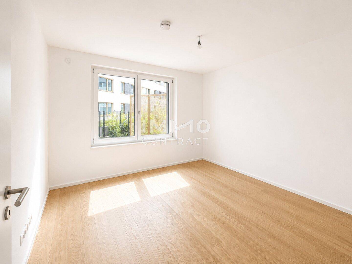 Ruhiges Schlafzimmer mit Holzboden und Fenster mit Blick auf eine grüne Außenanlage.