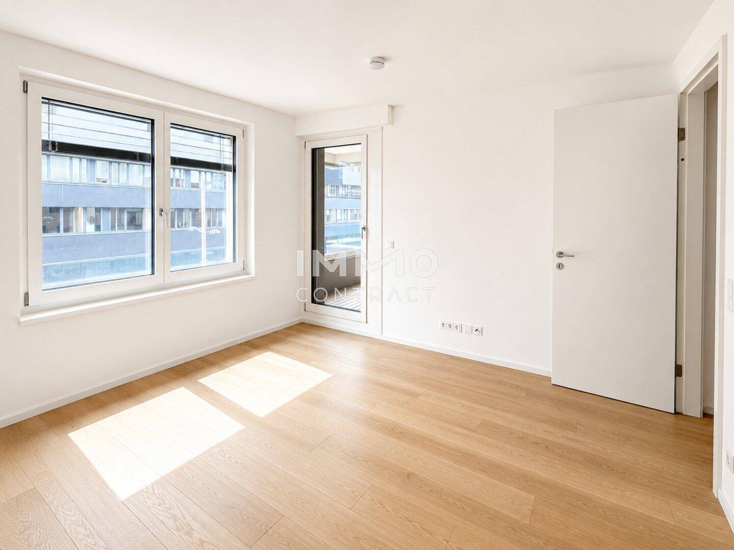 Helles Schlafzimmer mit Holzboden, Fenster und Zugang zu einem kleinen Balkon.