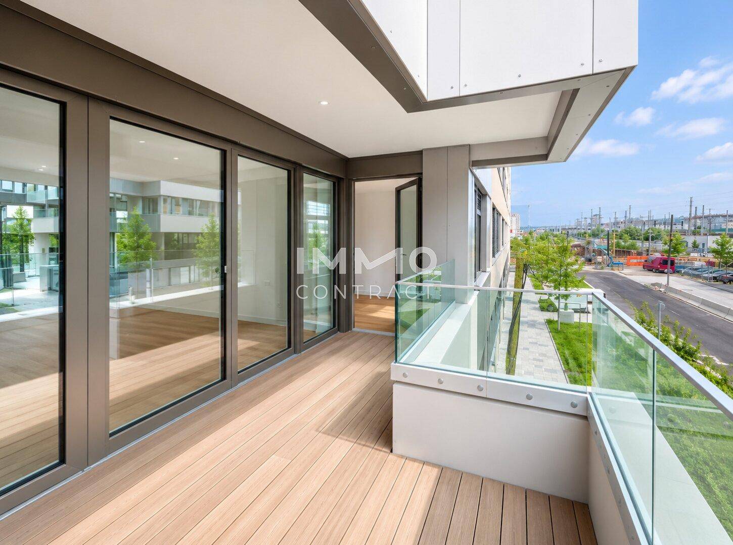 Geräumiger Balkon mit Holzdeck, Glasgeländer und Blick auf die Stadt.