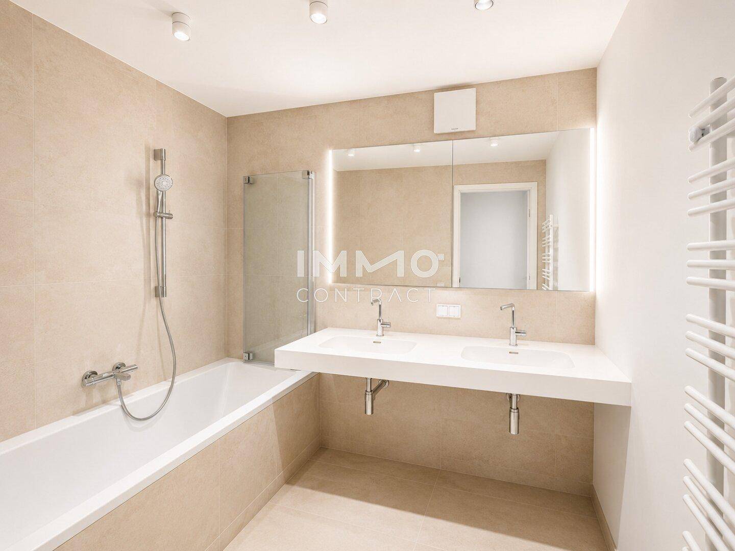 Modernes Badezimmer mit beigefarbenen Fliesen, Doppelwaschbecken und Badewanne mit Duschfunktion.