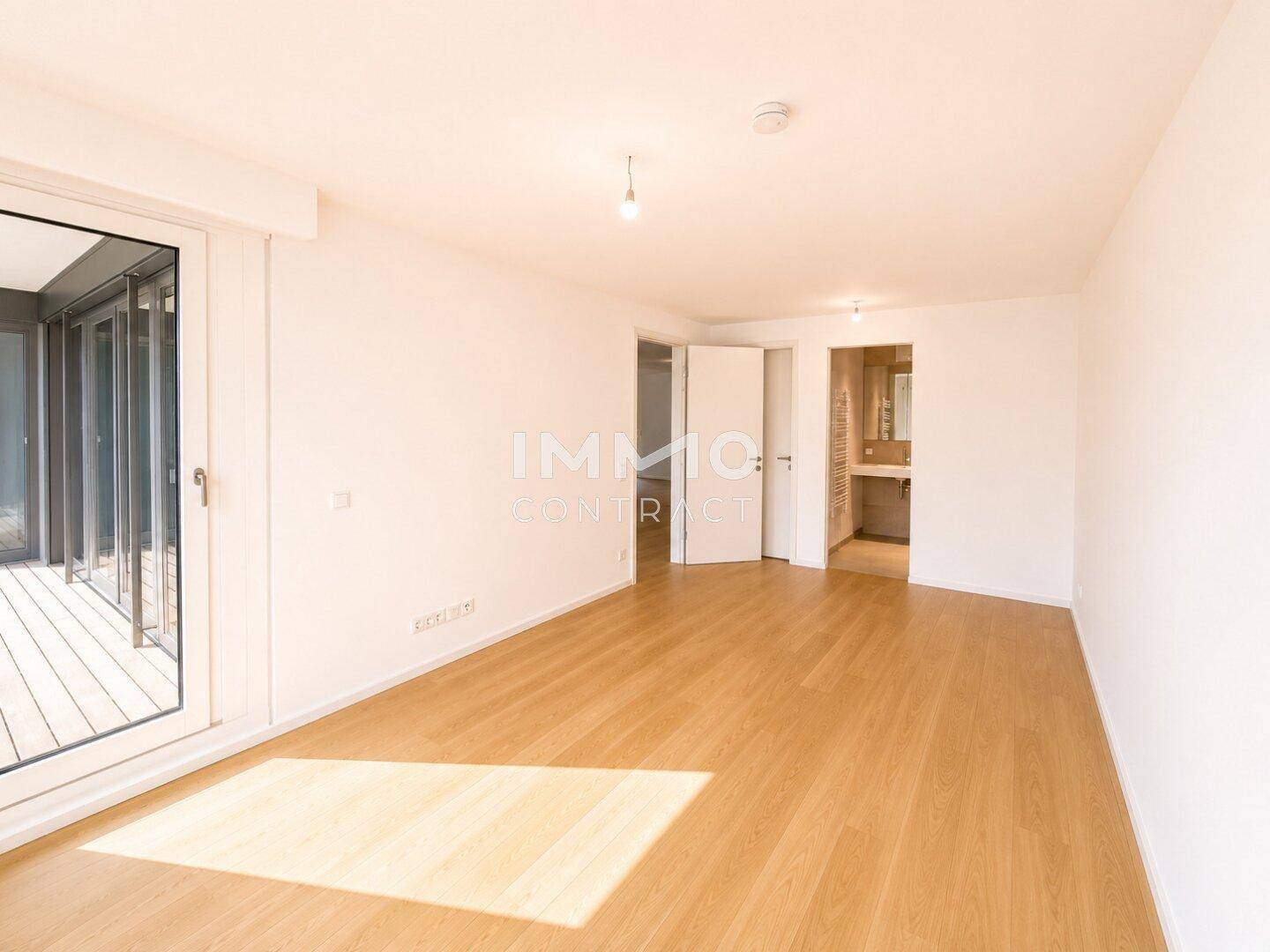 Helles Zimmer mit Holzboden und Zugang zu einem Außenbereich, mit Blick auf das angrenzende Badezimmer.