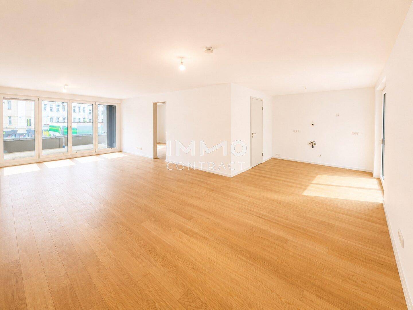 Geräumiger, heller Wohnbereich mit Holzboden und großen Fenstern, die viel Tageslicht hereinlassen.