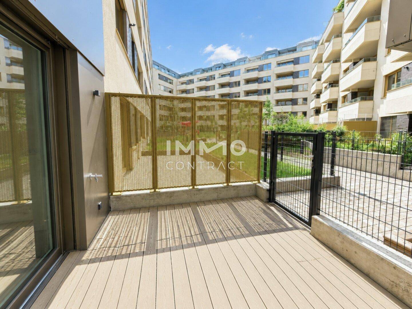 Moderne Terrasse mit Holzdielen und Blick auf den begrünten Innenhof eines Wohnkomplexes.