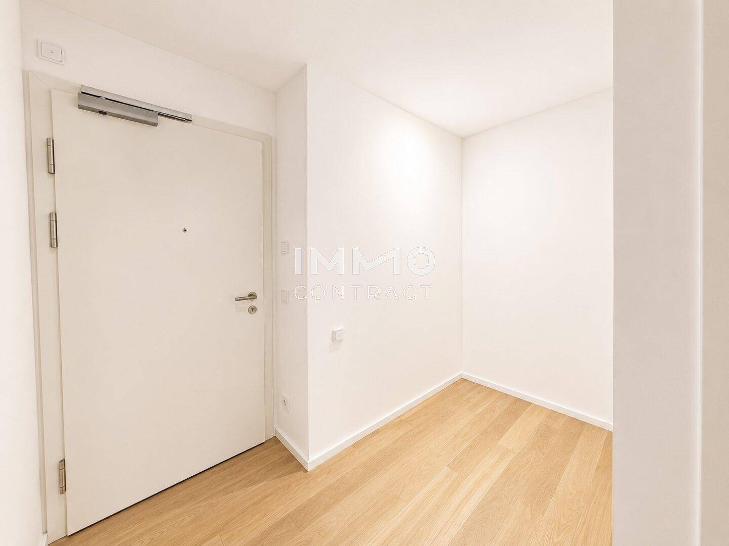 Heller Eingangsbereich mit Holzboden und weißer Tür, der einen modernen und sauberen Eindruck vermittelt.