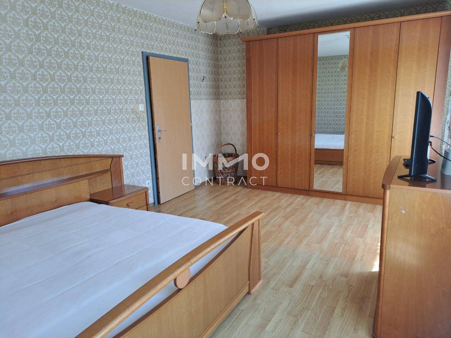 Schlafzimmer mit großem Kleiderschrank, Holzbett und Laminatboden.